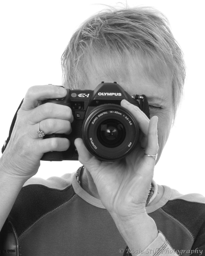 A black and white studio portrait of me behind my first digital camera, the Olympus E-1